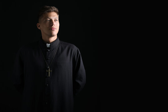 Priest in cassock with cross on black background. Space for text