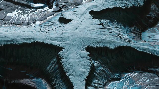 The image shows a large glacier formation with visible lines and cracks. The uneven surface displays a mix of dark and light shades. Ice flows create various patterns across the landscape.