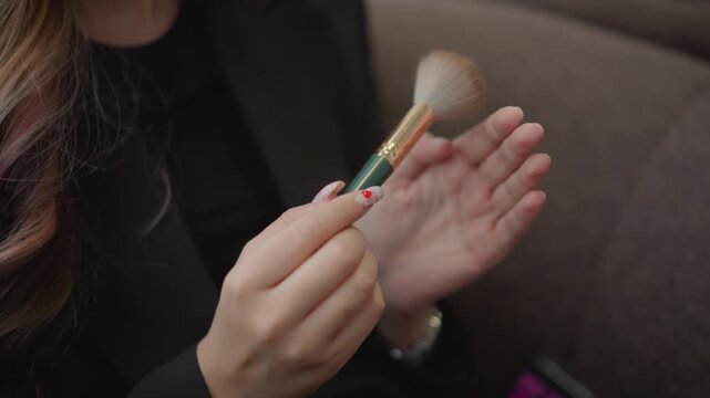 Close-up shows hands tapping soft makeup brush onto back of other hand to test powder texture and pickup, with gentle downward movement, visible bristles, and calm indoor beauty routine