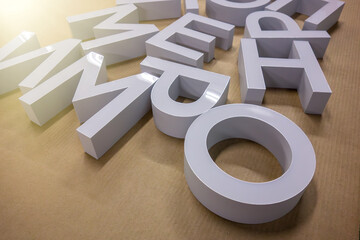 Fototapeta premium White 3D letters lying on a surface. Large plastic signage characters for advertising or storefront branding. Alphabet elements for design, typography, communication and marketing.