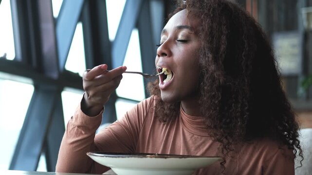Beautiful African American woman eating pasta with seafood in a restaurant. Woman enjoying food. Close-up