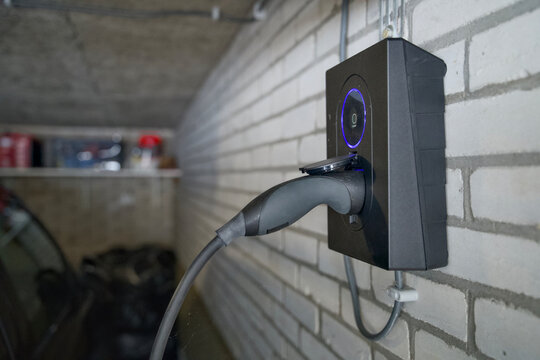 close up of hand plugging electric vehicle charging cable into home wallbox charger, electric driving and energy transition concept