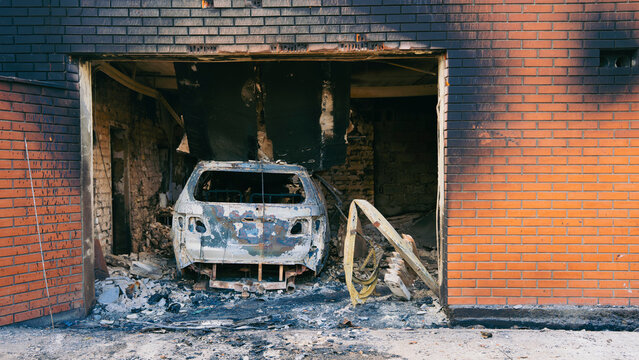 A burnt out car and destroyed garage inside a damaged brick building following shelling and fire caused by war conflicts