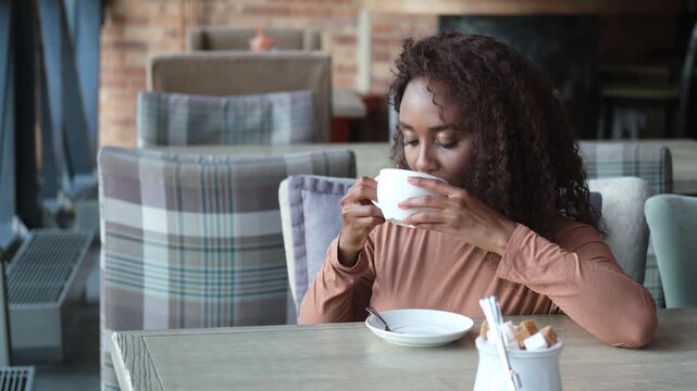 A very beautiful African American woman is sitting at a table in a cafe with a cup of coffee or tea.