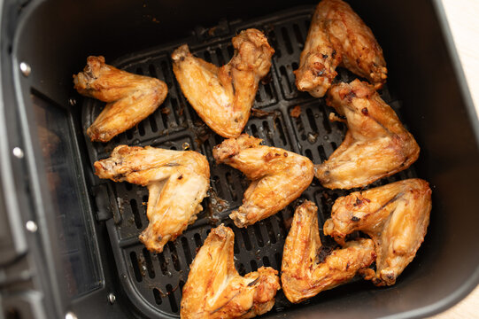 Crispy golden chicken wings cooked in an air fryer basket. Concept of homemade food, air frying, quick cooking and preparing chicken with less oil.