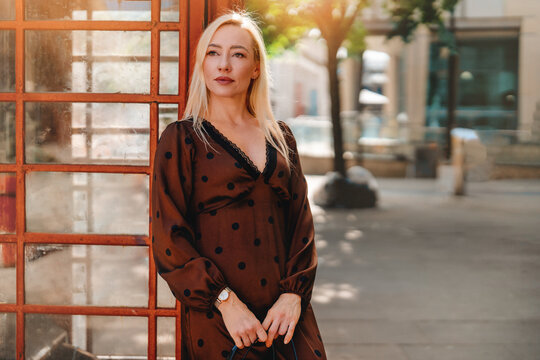 Woman standing near a red phone booth in an urban setting during sunny weather
