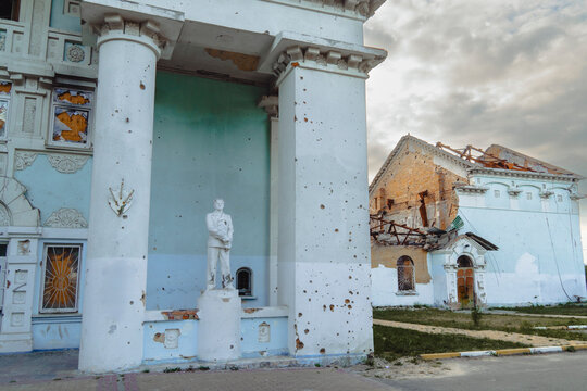 Damaged heritage building with shrapnel marks on white columns and standing statue after military shelling during armed conflict