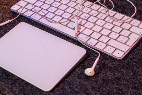 Top view of a white wireless keyboard, trackpad and wired earphones on a dark felt desk mat in purple light