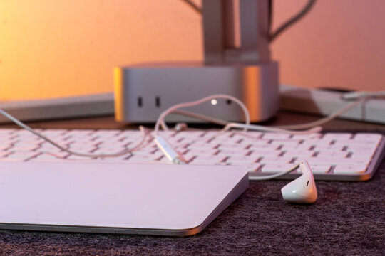 White wired earphones on a keyboard and trackpad with a silver mini computer glowing in warm light behind