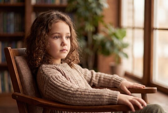 Thoughtful curly girl sitting by window cozy interior warm light