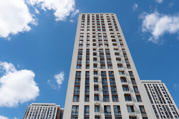 Fototapeta premium Looking up at a tall modern high-rise apartment building against a bright blue sky with white clouds in the city