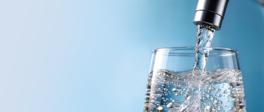Crystal clear water pouring into a glass against a bright blue background, symbolizing freshness and purity