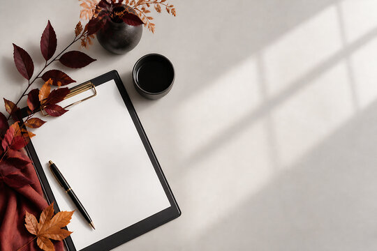 A flat lay composition featuring a clipboard with a pen, dark decorative elements, and a small bowl on a light-colored surface.