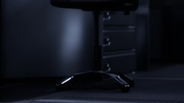 An office space shows a black swivel chair near a cabinet. The lighting creates shadows, highlighting the floor markings. The setting feels modern and slightly mysterious.