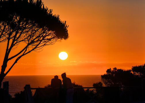 Couple watching the sunset on La Barrosa beach, Chiclana, Spain.