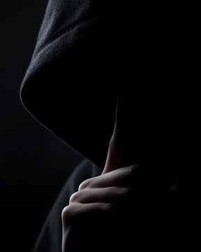 hooded figure demanding silence with finger on lips mysterious hacker concept