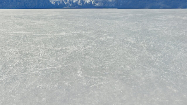 a large, natural expanse of ice. Scratched ice surface texture. Blue ice background with skate traces, cracks, scratches. Rough winter sport rink backdrop.