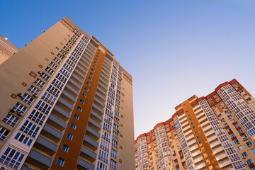 Fototapeta premium Low angle view of modern high rise residential apartment buildings in complex with windows and balconies against clear blue sky in modern city district
