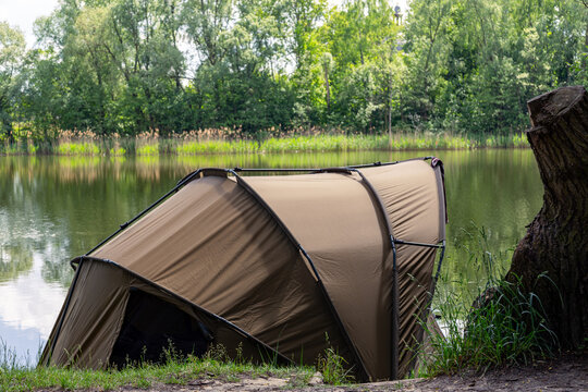 Carp fishing bivvy set up by lake shore with trees and calm water