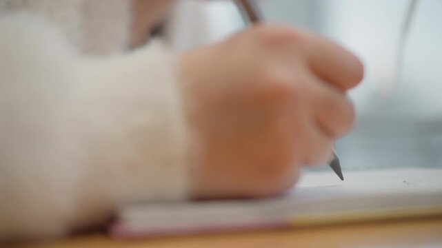 Tight low-angle view of hand holding pen while writing on paper at desk, with visible pen tip movement, soft natural light, shallow depth and quiet workspace mood, with hand, pen, writing, paper