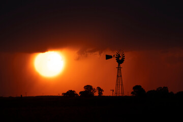 Naklejka premium Windmill at sunset with a rain storm in the background, Pampas, Patagonia,Argentina.