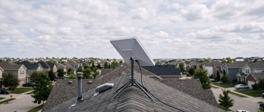 Satellite internet antenna mounted on residential rooftop overlooking suburban neighborhood and cloudy sky