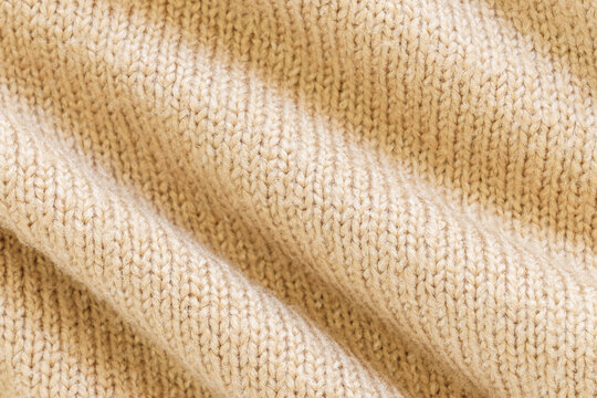 Closeup of soft beige knitted textile with flowing folds, warm sunlit highlights, and detailed yarn structure, creating cozy background suitable for fashion, home decor, and seasonal design themes