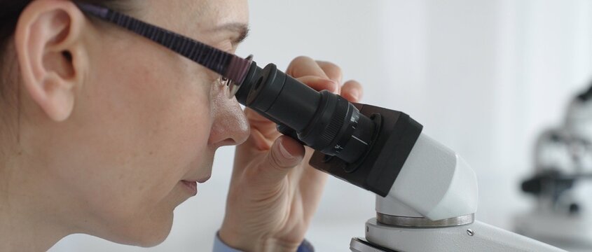 Female researcher focusing on a microscope lens, analyzing scientific samples in a sterile lab for medical innovations. Medicine and science concept