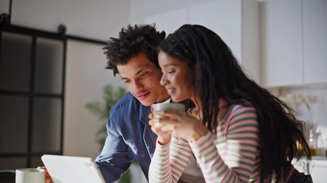 Two spouses looking tab screen holding coffee talking in modern kitchen closeup