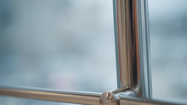 Close-up view of polished stainless steel handrail where vertical post meets horizontal bar, showing rounded connector, reflective streaks, cool blue-gray tones, and gentle motion blur