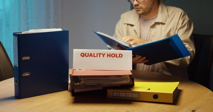Worker reviewing documents marked Quality Hold. Ideal for quality control, inspection, nonconformance, manufacturing and compliance.