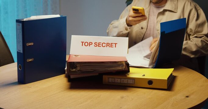 Person secretly photographing Top Secret documents with a smartphone and flash. Ideal for data theft, corporate espionage, security breach and confidential information.