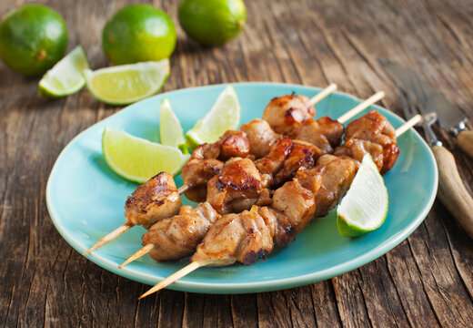 Close-up of a Plate of Mahogany Chicken Skewers with fresh lime on a wooden table