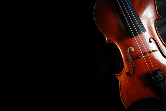 A polished wooden violin against a deep black background, highlighting its elegant curves, strings, bridge, and rich warm tones with dramatic studio lighting and ample copy space.