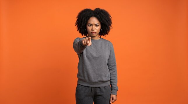 Serious Young Black Woman Pointing at Camera with Accusing Gesture on Orange Studio Background