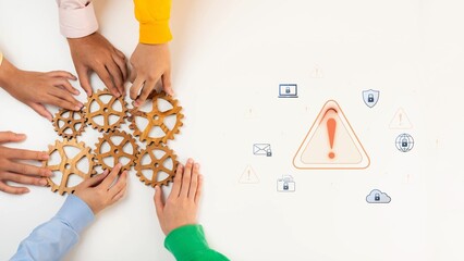Obraz premium A diverse group of hands gathers around gears on a table, symbolizing teamwork and collaboration. A warning icon highlights communication and cybersecurity issues in today work environment. Raster
