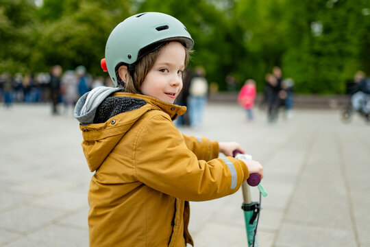 Young boy wearing a safety helmet rides a kick scooter on a city sidewalk. Active childhood, urban mobility and road safety for children.