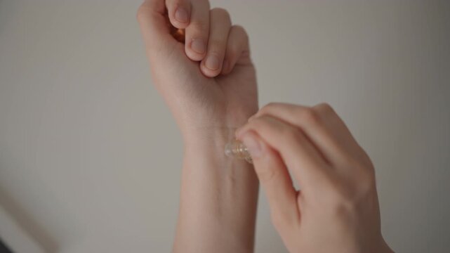 Close-up view of hands applying transparent adhesive patch to inner wrist while fingers peel backing, press edges, smooth surface, and flex wrist gently under soft warm light, with hand, wrist