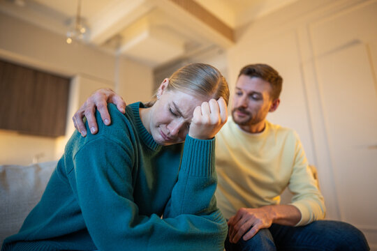 Married couple sitting on couch together after quarrel, crying woman distancing from unfair husband, toxic anxious partner embracing and calming unhappy wife, betrayal, complex discussion and crisis.