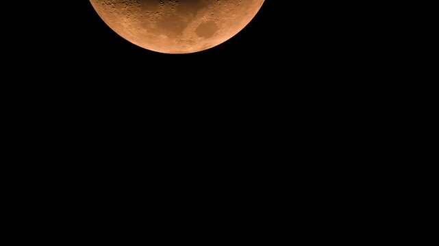 Close up view of orange crescent moon moving across dark night sky