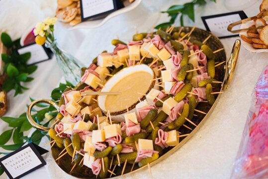 Charcuterie board arranged, in indoor, with cheese, meats, fruits, herbs, with brown, white accents.