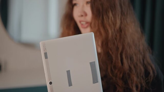 Young woman holds and adjusts handheld garment steamer at chest level while looking down with focused expression, head tilt and steady grip suggesting careful inspection before steaming clothing