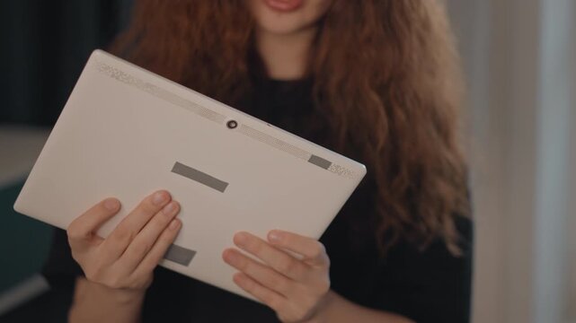 Smiling woman in softly lit indoor setting holds white spiral bound sketchbook at chest level, then lowers it toward viewer while covering mouth, showing playful shyness and calm focus