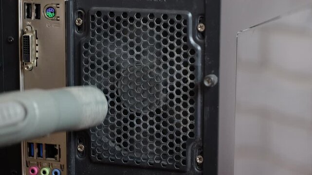 Cleaning dust from computer power supply fan. Close-up of a technician using a vacuum cleaner to remove dust and dirt from the back panel fan grill of a desktop computer, ensuring proper ventilation