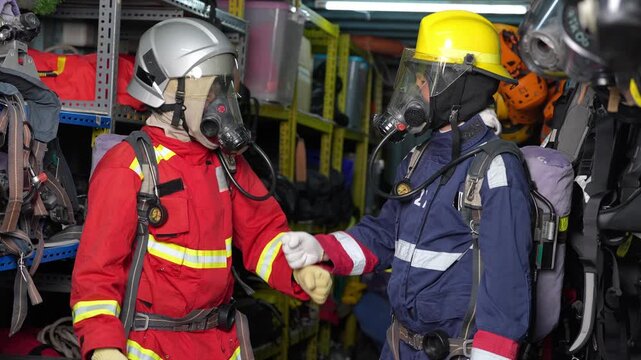 Firefighter rescue teamwork training with breathing apparatus gas mask helmet safety inside equipment room, emergency responders in protective gear with air tank, fist bump readiness