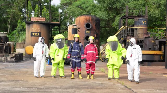 Hazmat suit firefighter rescue team training at industrial facility, protective worker line walk near tanks, refinery yard confined space station, emergency response drill