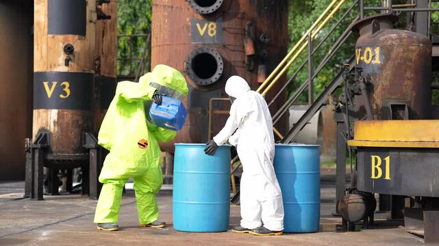 Hazmat suit hazardous waste chemical drum industrial plant spill response contamination safety cleanup, workers handle toxic barrel during refinery yard emergency drill with caution