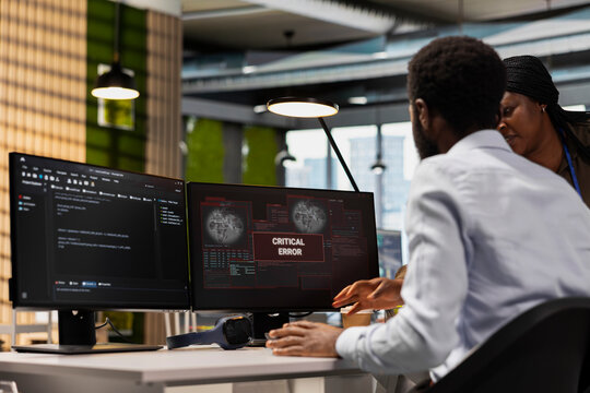 System administrators collaborate in an office to fix a critical error warning, brainstorming solutions and troubleshooting the glitch notification on a computer screen during incident response.