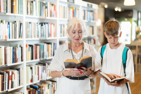 Smiling grandmother with grandson holding a book in public library with large stock