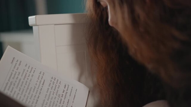 Over-shoulder close-up shows person leaning toward handwritten notebook, gently turning page while studying notes with calm reflective posture in soft indoor light, with notebook, reading